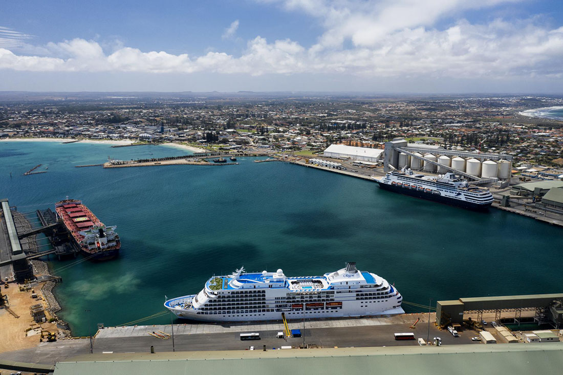 Two cruise ships and one cargo ship berthed in port. View of city in background.