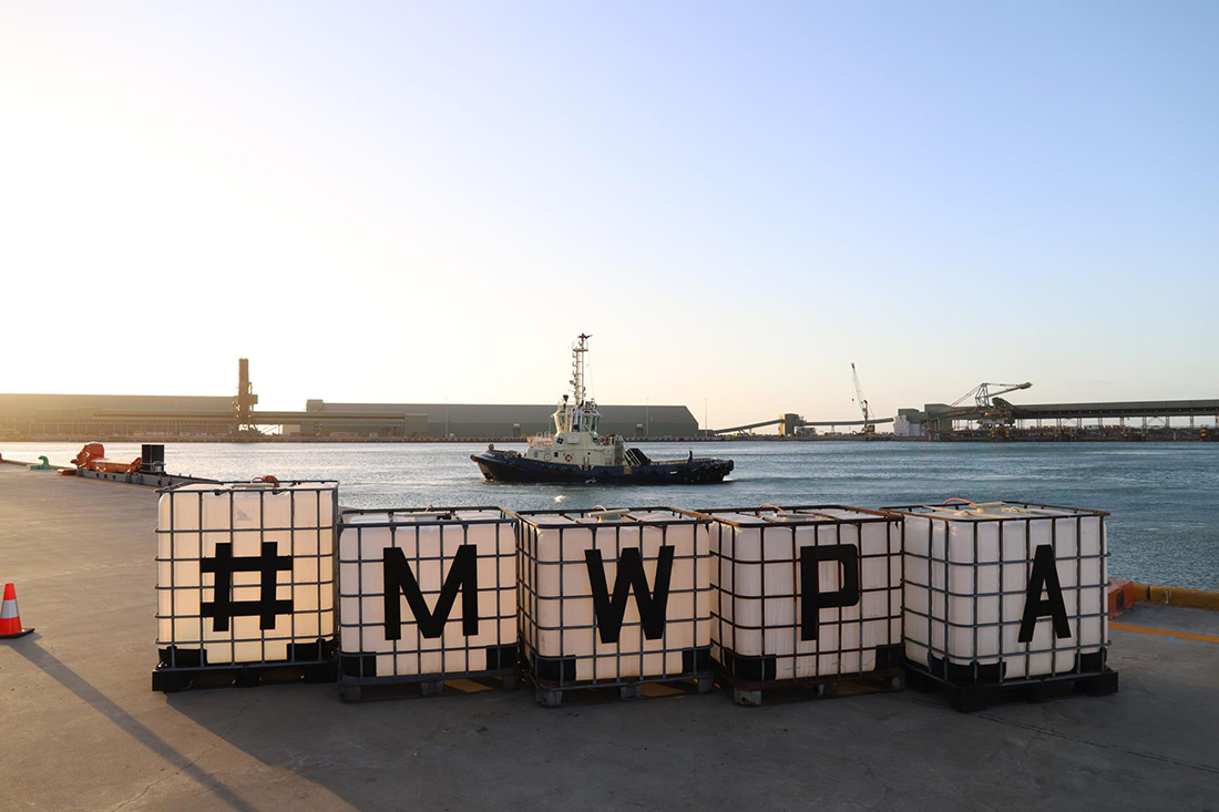 Four large containers with a character on each spelling #MWPA positioned in front of tug boat and port