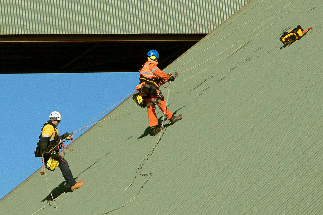 Two people using ropes to climb green slanted roof