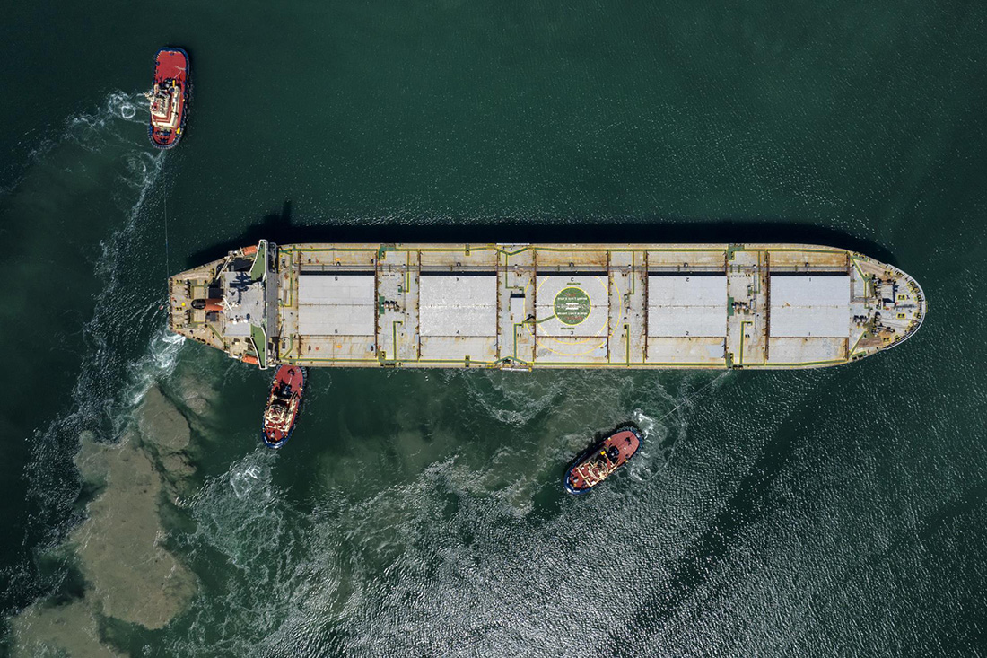 Overhead view of cargo ship with three tugboats
