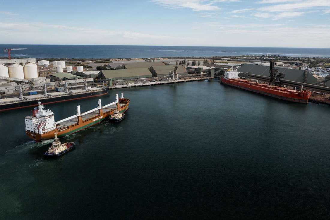 Port area with two cargo ships. One is being accompanied with two tugboats.