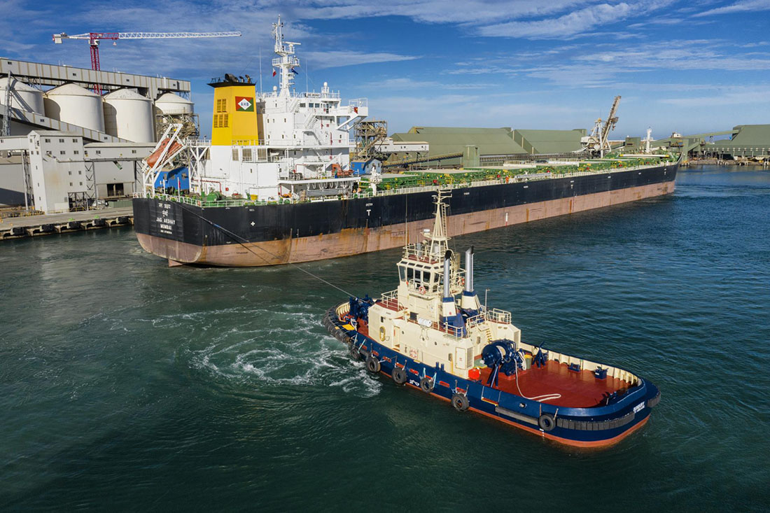 Sideview of cargo ship being pulled by tug boat.