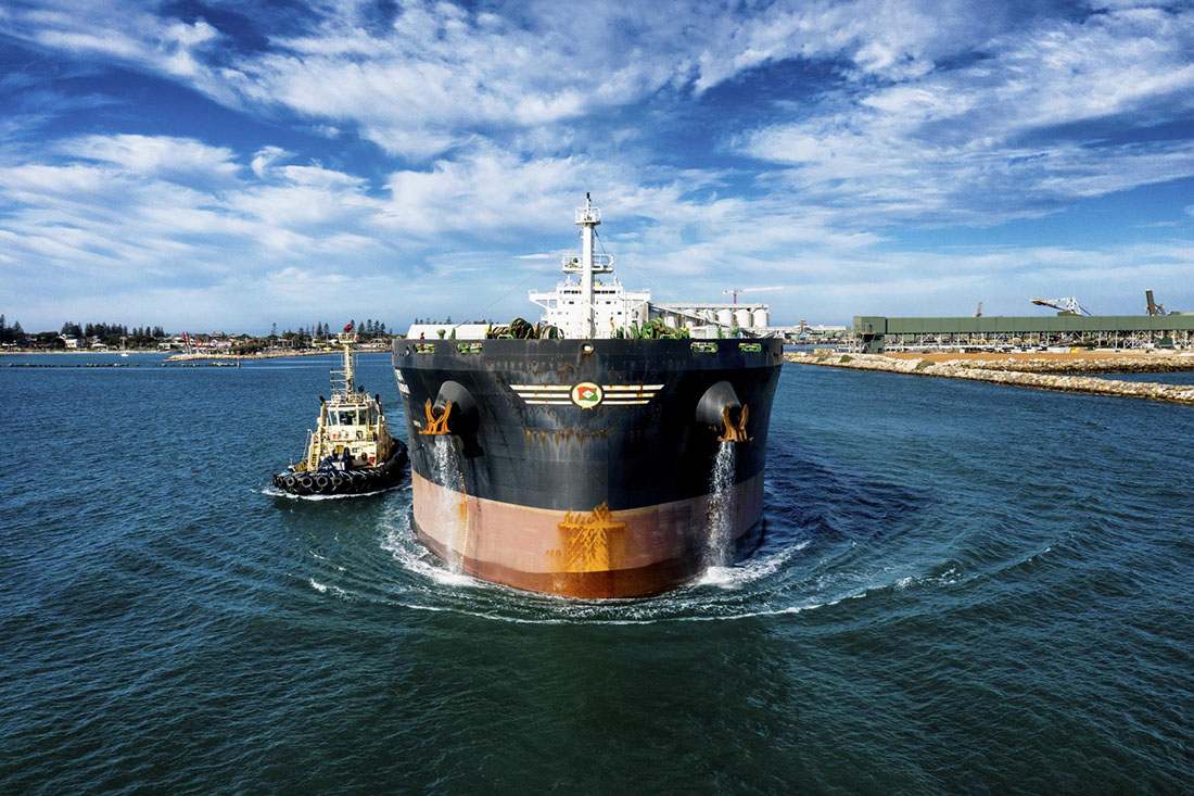 Front view of cargo ship with a tugboat along side on the left.