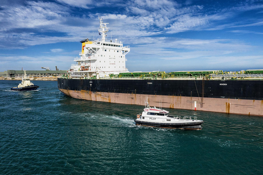 Cargo ship exiting port with a pilot boat and tugboat accompanying it.