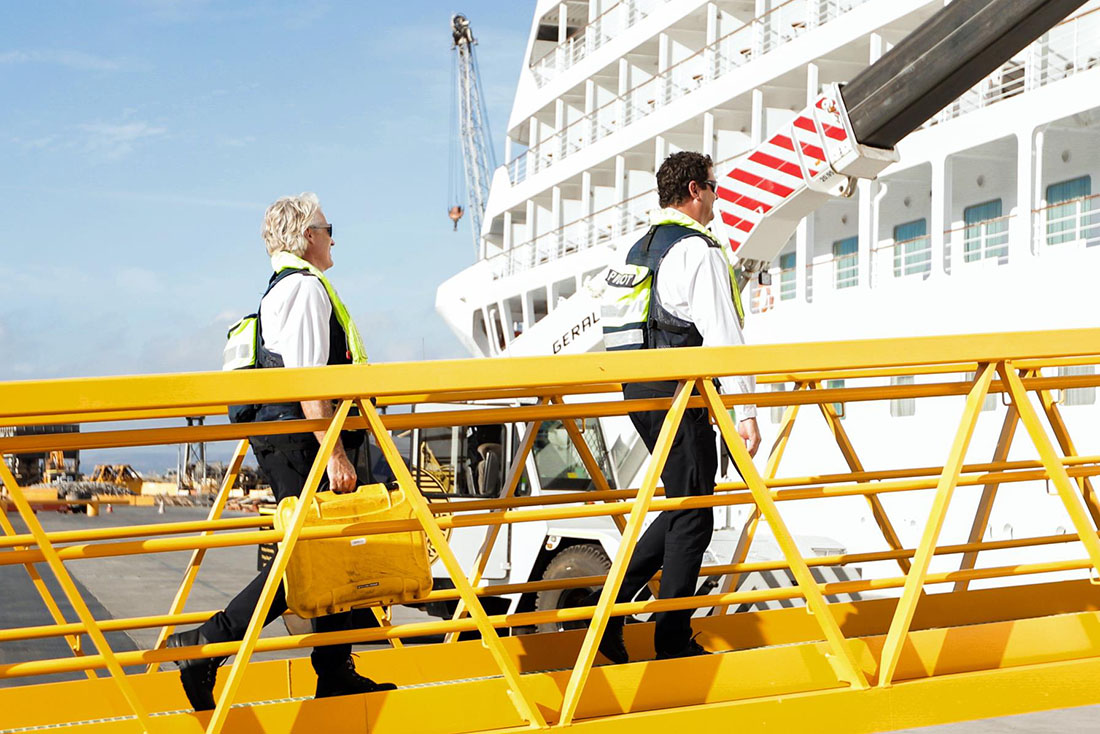 Two ship pilots walking on yellow bridge towards cruise ship