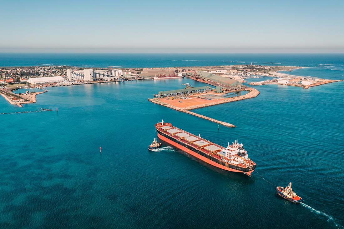 Overview of port looking south. One cargo ship and two tug boats head into port.