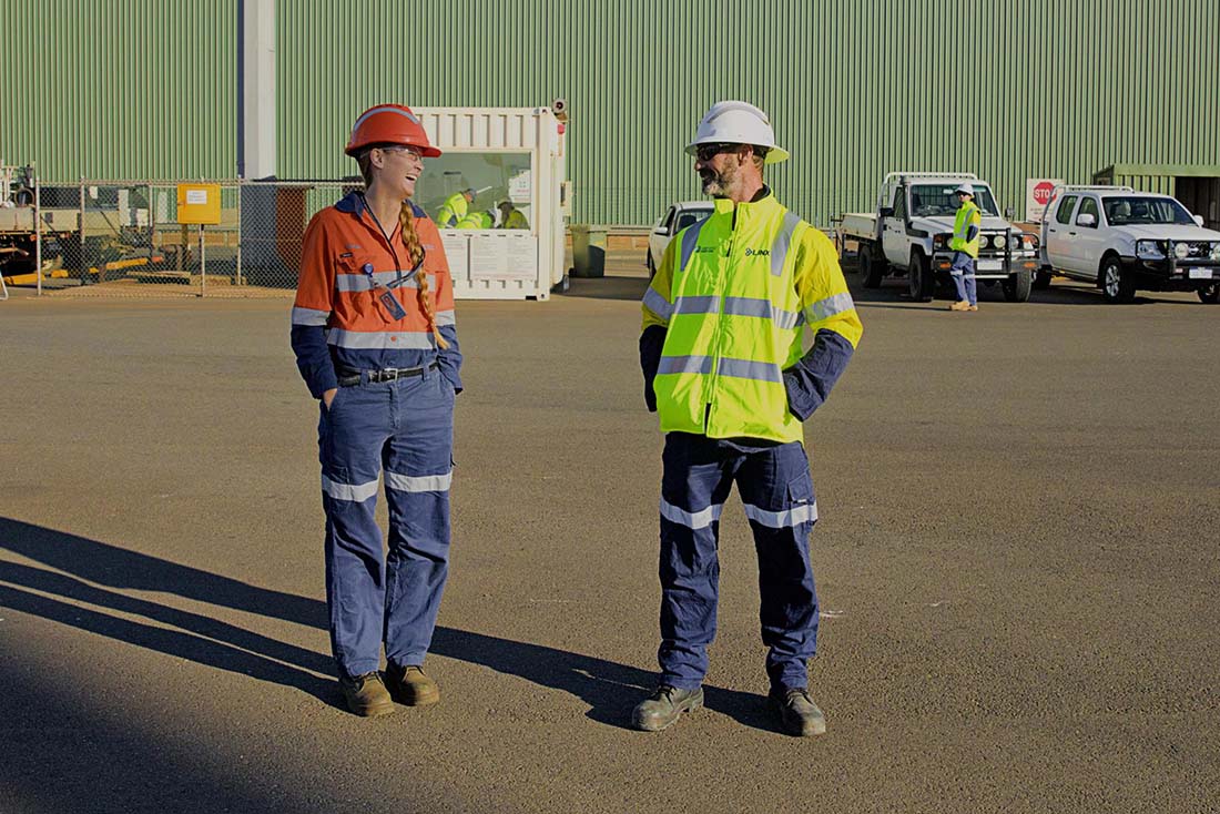 Two staff members smiling while speaking in front of a green shed