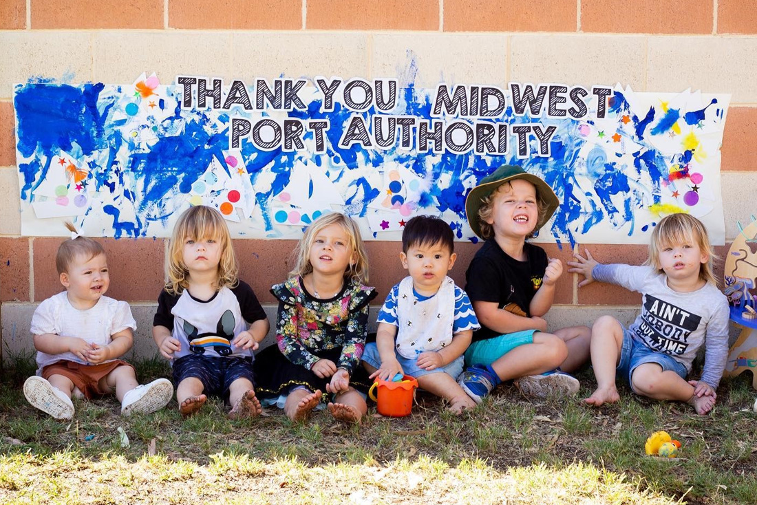 Six young children sitting in front of wall with abstract painting behind them.