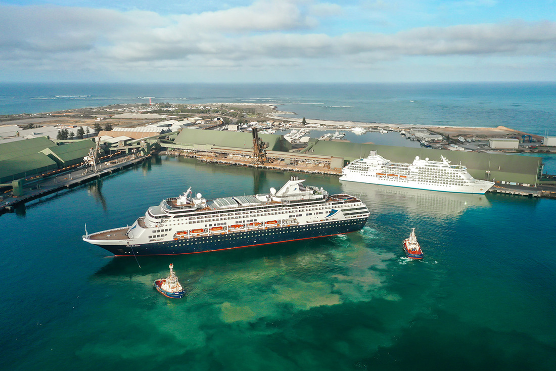 Two cruise ships in port. One being guided by two tug boats.