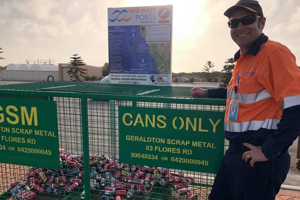 Man standing beside metal cage full of soft drink cans.